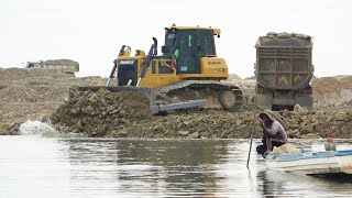 Big lake filling using rock and dirt bulldozer working with 10 wheels dump truck