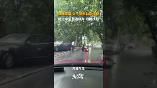 雨天路滑，女子骑电动车摔倒。路过的车主靠边停车，下车把她扶起来。