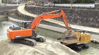 Japanese hydraulic excavators dig up river sediment.