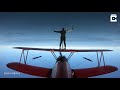 daring guy stands on top of flying plane