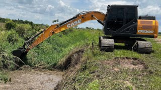 Escavadeira Hidráulica em Ação: Limpeza de Valeta Tomada pelo Mato