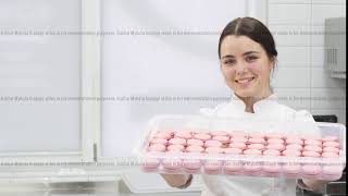 Professional confectioner smiling holding out tray full of macaroons to the camera