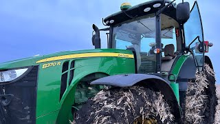 John Deere 8370R tractor works after corn on wet terrain.