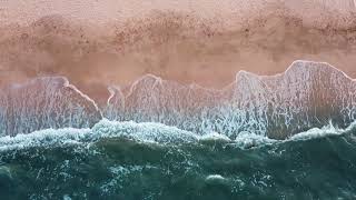 Sandy beach and blue sea, foaming waves on the coast. Aerial view from above. Drone footage