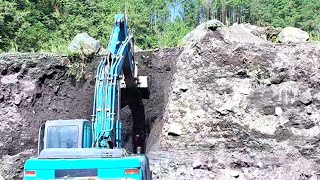 Kobelco excavator works cutting sand cliffs then loading them into the bed of a truck - 4k