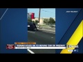 woman holds on to moving car on freeway