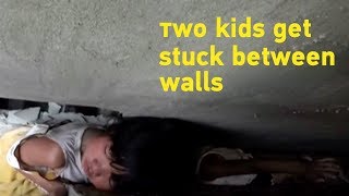 Two playful kids get themselves stuck between narrow walls