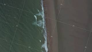 Slow Aerial Overhead Top Down Birds Eye View of Green Ocean Water and Brown Beach