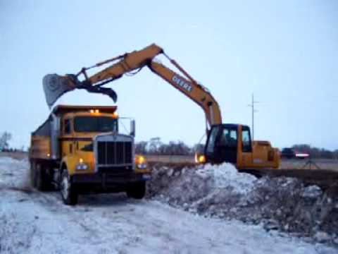 EXCAVATOR LOADS DUMP TRUCK WHILE BUILDING A BERM - YouTube