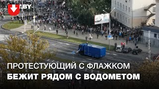 Протестующий с флажком бежит рядом с водометом в районе ул. Тимирязева