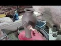 trimming and slip decorating a tall jar vase on the potters wheel.