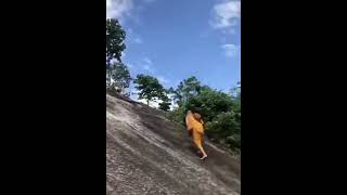 A monk climbing with bare feet on the cliff that tourists climb on with the help of a rope