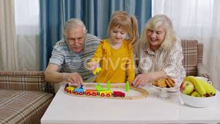 Mature Couple Grandmother Grandfather with Child Girl Grandkid Riding Toy Train on Railroad at Home