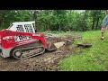 tracked skid steer digging out and moving big rocks smooth bucket