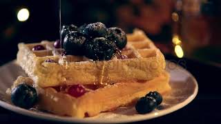 Selective focus of viscous honey dripping on Belgian waffles with blueberries