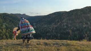 Siberian shaman performs a ritual dance and beats a tambourine on the top of the mountain.