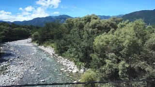 夏晴れの中央アルプスと農村風景を見ながら飯田線の大田切駅に到着する上り313系の車窓