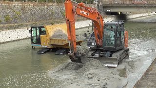 Japanese hydraulic excavators dig up river sediment.