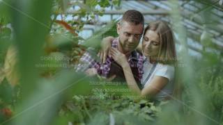 Cheerful woman embrace and kiss husband watering flowers with garden pot. Happy young florist couple