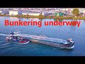 Inland cargo ship ''Sagrada'' taking bunkers underway in Netherlands inland waterway. Aerial video.