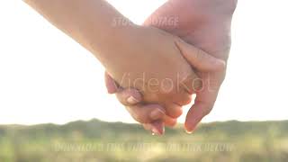 A man and a woman walking holding hands in a summer field on sunset background in slow motion