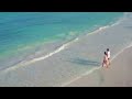 young couple walks into waves on tropical beach by aerial drone hd