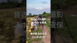 「アイリスブリッジ(赤い橋)」と「北潟湖」。皆さん花火撮影ポイントを確保。アイリスブリッジは、北潟湖畔公園と花菖蒲園をつないでいる橋で、1999年に全面開通。福井県 あわら市。2024年9月7日。