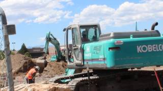 2 Blue Kobelco Excavtors working digging a hole on a construction site